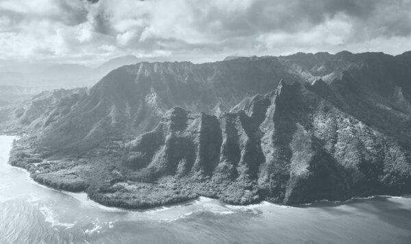 Black-and-white aerial view of steep, ridged Hawaiian sea cliffs meeting the ocean under heavy clouds