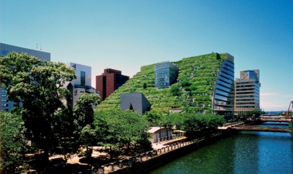 Terraced green-roofed building planted with trees and shrubs rising above a river and city skyline