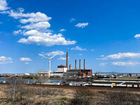 A large, fossil gas-fired power plant in Massachusetts next to a wind turbine with the Tobin Bridge in the background.