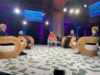 Five panelists sit in chairs in a semi-circle on a stage