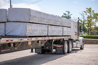 A white flatbed semitrailer loaded with pallets of OnWood wrapped in white plastic.