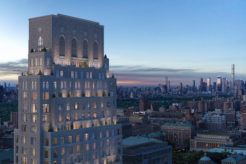 a tall stone building with a tapered design, lit up at dusk with the skyline of New York City behind it.