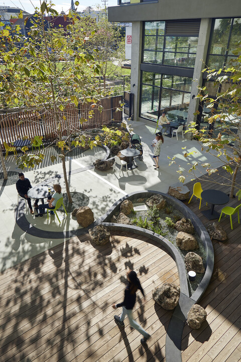 View from above the patio area of a multifamily building, with people, outdoor tables, and trees.