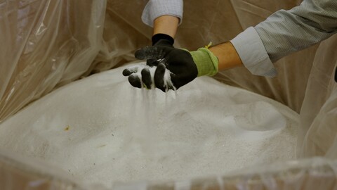 Two gloved hands reaching into a container of white sand.
