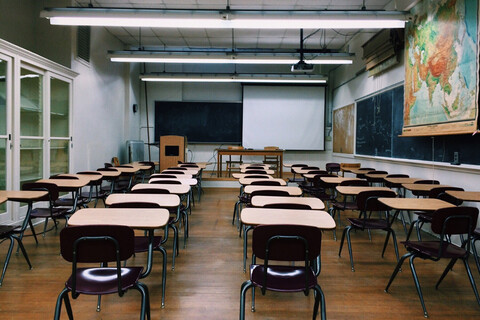 Empty classroom with rows of desks, chalkboards covering the walls, a pull-down world map and no visible windows.