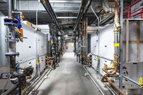 looking down an aisle of a mechanical room with ground-source heat pumps on either side.
