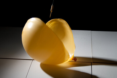 High-speed photograph of a yellow balloon being popped by a dart on a tile floor