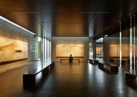 A visitor sits in a warmly lit gallery space.