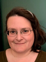 a slightly smiling person with dark shoulder-length hair and glasses